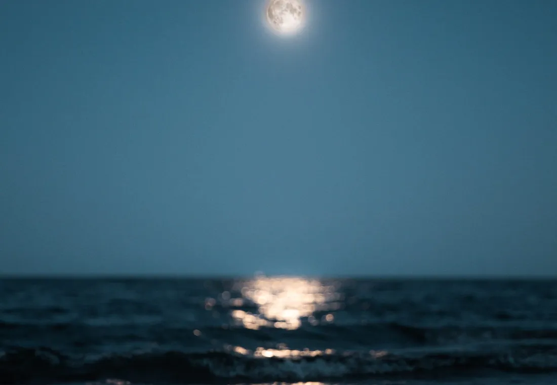 Calm sea with waves reaching the shore towards you with the wavy reflection of the full white moon