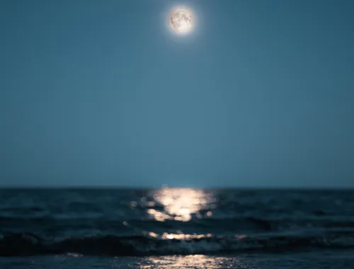 Calm sea with waves reaching the shore towards you with the wavy reflection of the full white moon