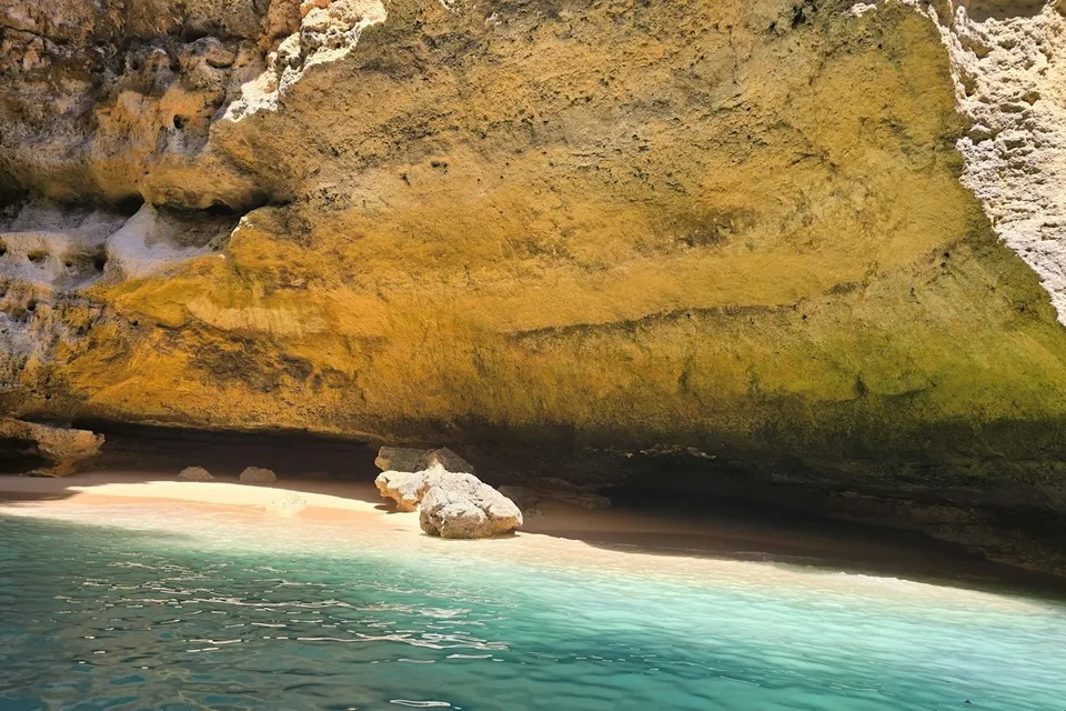 A sea cave with a sandy floor and turquoise water in the Algarve. Photo via Unsplash