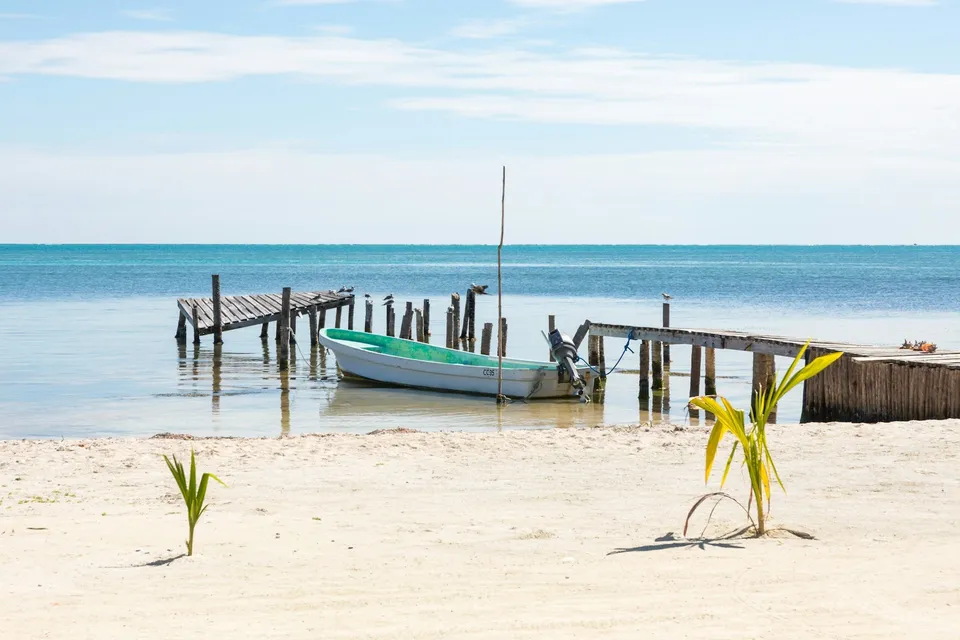 A boat by a wooden dock on a white sand beach in Belize. Photo via Unsplash