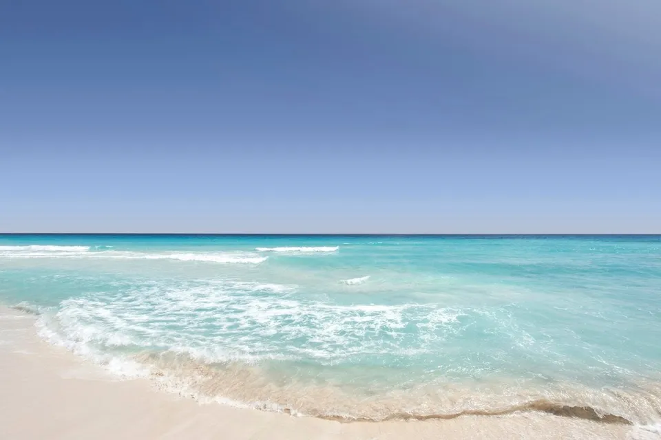 Clear blue sea washing on a sandy shore in Cancún. Photo via Unsplash