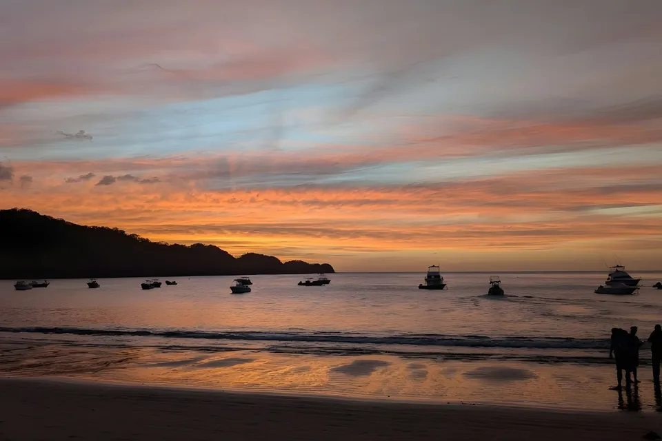 A sunset at the beach with boats on the water in Costa Rica. Photo via Unsplash