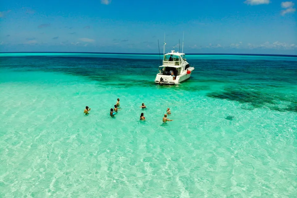 People swimming near a white boat on a turquoise sandbar, Cozumel. Photo via Unsplash