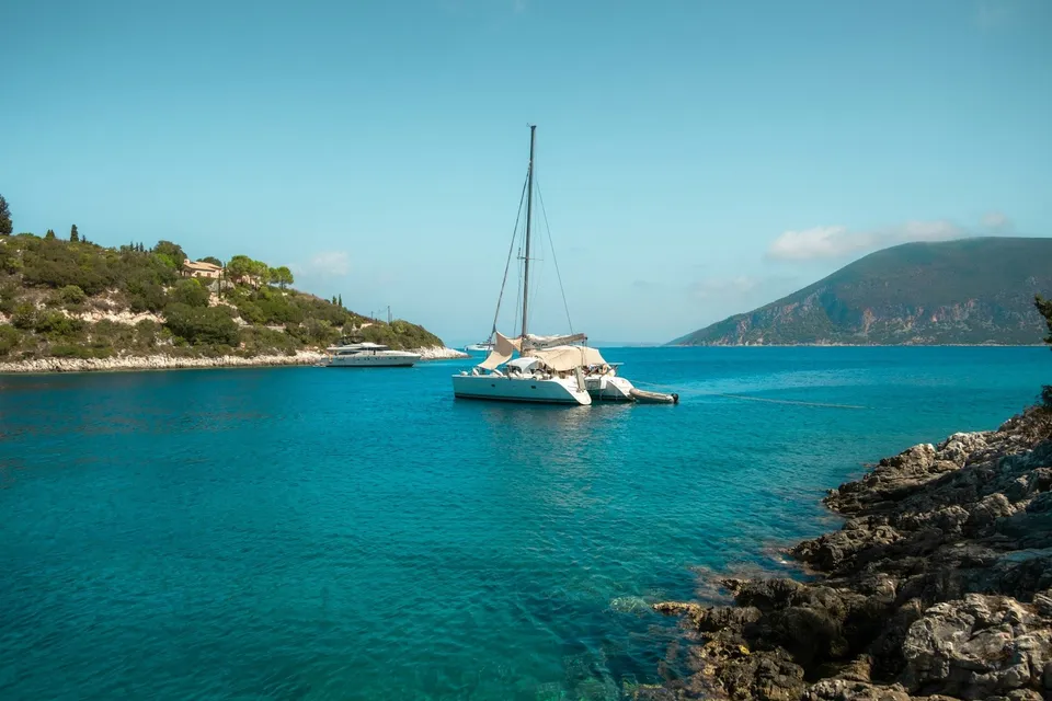 A catamaran in clear water by a rocky shore in the Ionian Sea. Photo via Unsplash