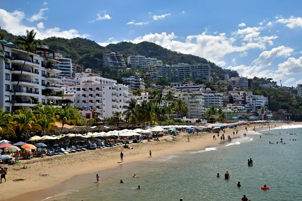 Beach with umbrellas and the hills of Puerto Vallarta in the background. Photo via Unsplash