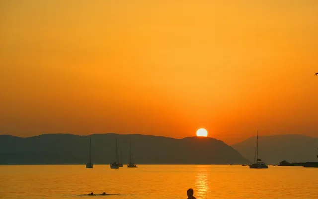 Sun setting behind mountains with sailboats at anchor
