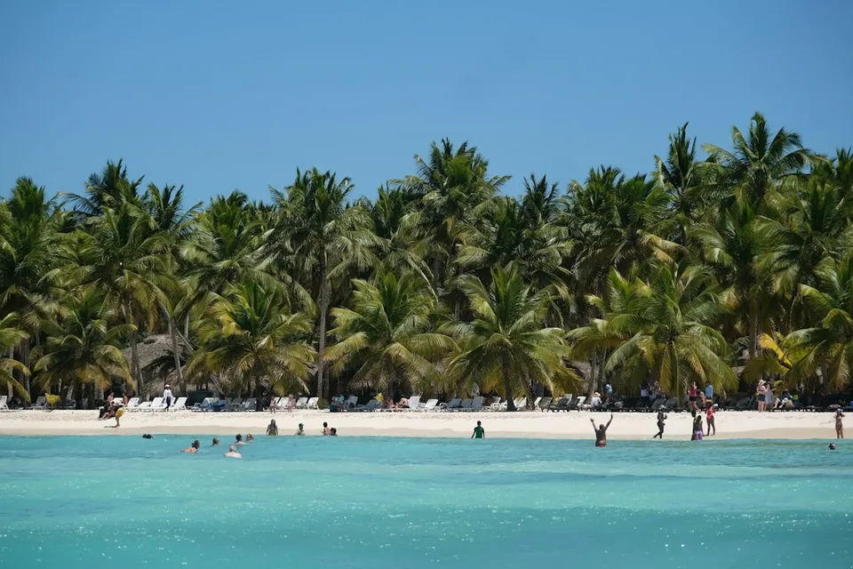 White-sand beach with palm trees and swimmers in turquoise water, Dominican Republic. Photo via Unsplash