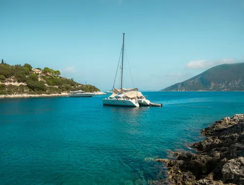 Catamaran in clear water by a rocky shore, Ionian Sea