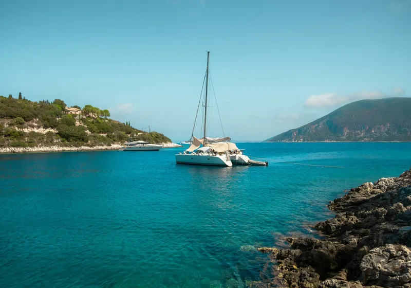 Catamaran in clear water by a rocky shore, Ionian Sea