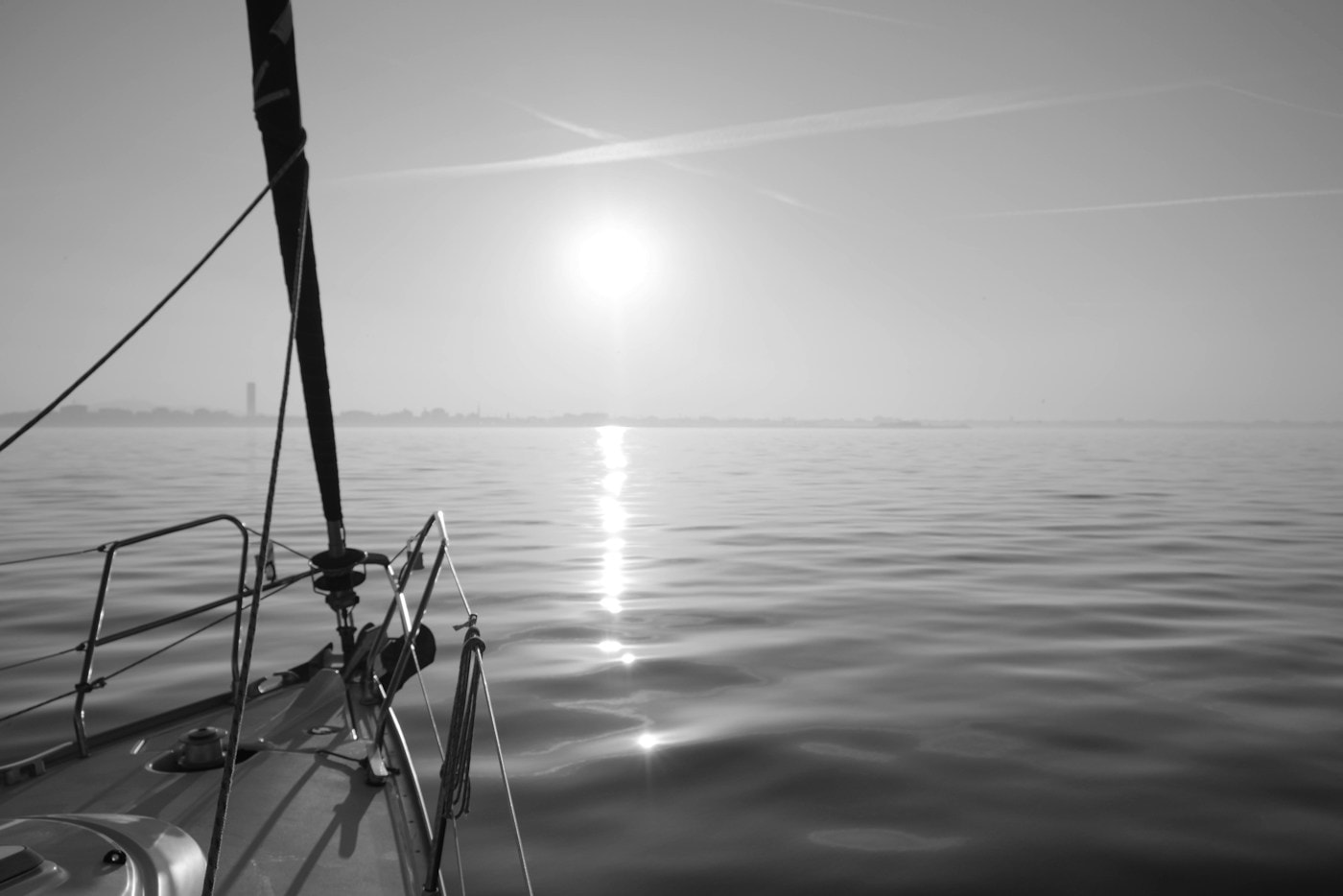 Bow of a sailboat at sunset with the sun reflected on the sea